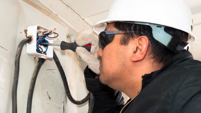 Ein Elektro-Installateur mit weissem Helm prüft die Kabel einer Steckose Ein Elektro-Installateur mit weissem Helm prüft die Kabel einer Steckose