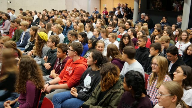 Junge Frauen und Männer versammelt in einem grossen Saal Junge Frauen und Männer versammelt in einem grossen Saal
