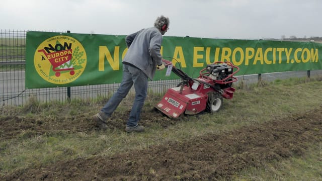 Ein Mann mäht Rasen vor einem Plakat. Ein Mann mäht Rasen vor einem Plakat.