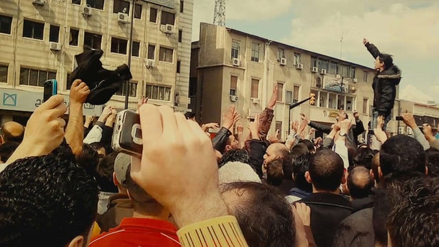 Filmszene: Eine Menschenmenge, vilee strecken die Arme in die Luft