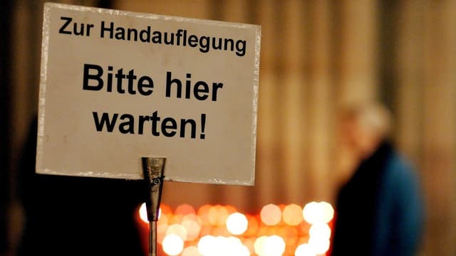 Ein Schild mit der Aufschrift: «Zur Handauflegung. Bitte hier warten!» Ein Schild mit der Aufschrift: «Zur Handauflegung. Bitte hier warten!»