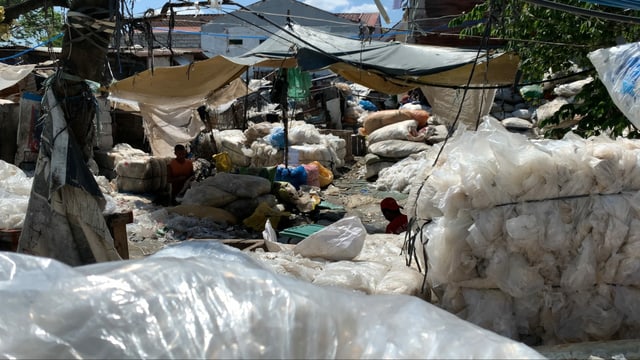 Die Umgebung in der NAchbarschaft ist voller Plastik. Im Vordergrund sind saubere Plastikballen im Hintergrund waschen sie Plastik unter einer Plastikplache Die Umgebung in der NAchbarschaft ist voller Plastik. Im Vordergrund sind saubere Plastikballen im Hintergrund waschen sie Plastik unter einer Plastikplache