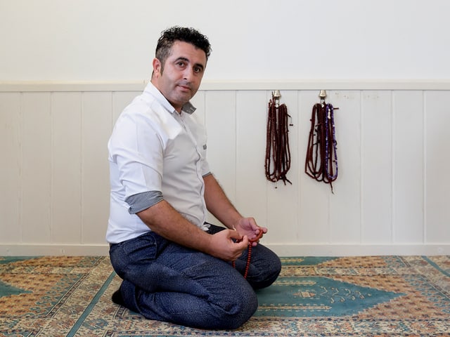 Ein Mann sitzt auf dem Teppichboden einer Moschee, in der Hand eine Gebetskette.