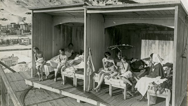 eine schwarz-weiss Fotografie von Holzblöcken im Freien und Frauen, die sich darin sonnen eine schwarz-weiss Fotografie von Holzblöcken im Freien und Frauen, die sich darin sonnen