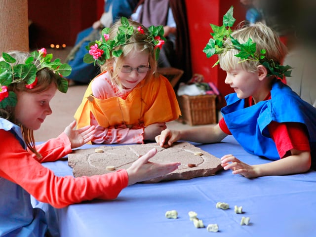 Drei Kinder sitzen an einem Tisch und spielen Mühle auf einem alten Stein. Drei Kinder sitzen an einem Tisch und spielen Mühle auf einem alten Stein.