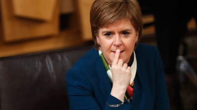 Sturgeon sitzt im Parlament, sie hält den Zeigefinger der rechten Hand an den Lippen. Sturgeon sitzt im Parlament, sie hält den Zeigefinger der rechten Hand an den Lippen.
