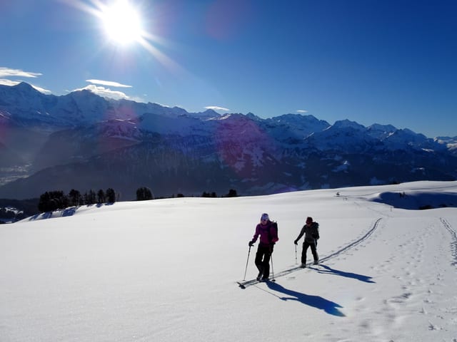 Tourengeher geniesen den Aufstieg im eher flachen Gelände, es liegt ausreichend Schnee, der Himmel ist mehrheitlich blau.