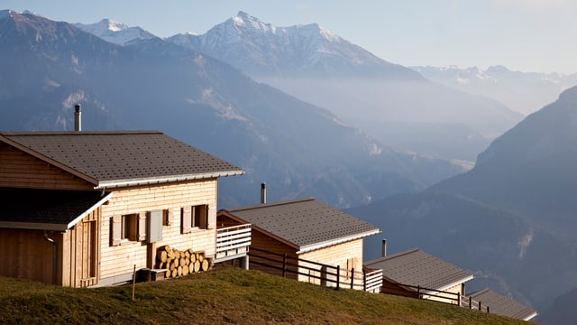 Drei Holzhäuser auf einer Bergkuppe. Im Hintergrund Berge. Drei Holzhäuser auf einer Bergkuppe. Im Hintergrund Berge.