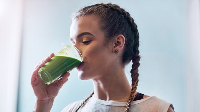 Eine junge Frau mit Zopf-Frisur trinkt ein grünes Getränk