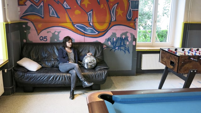 Eine Frau sitzt auf dem Sofa zwischen Töggelikasten und Billardtisch Eine Frau sitzt auf dem Sofa zwischen Töggelikasten und Billardtisch