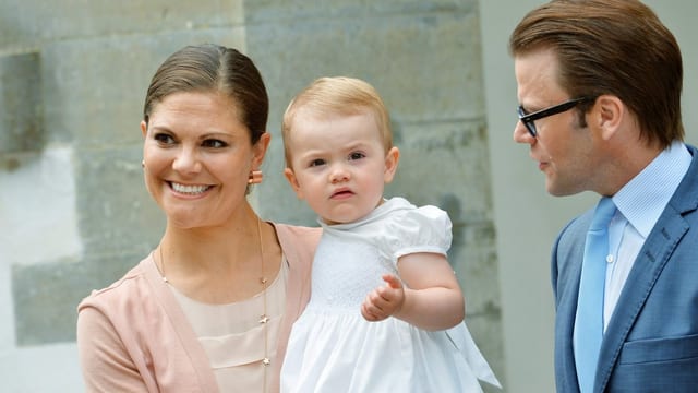 Victoria mit Estelle auf dem Arm. Prinz Daniel steht rechts von ihnen. Victoria mit Estelle auf dem Arm. Prinz Daniel steht rechts von ihnen.