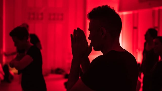 Ein Mann mit gefalteten Händen in einem rot beleuchteten Saal Ein Mann mit gefalteten Händen in einem rot beleuchteten Saal