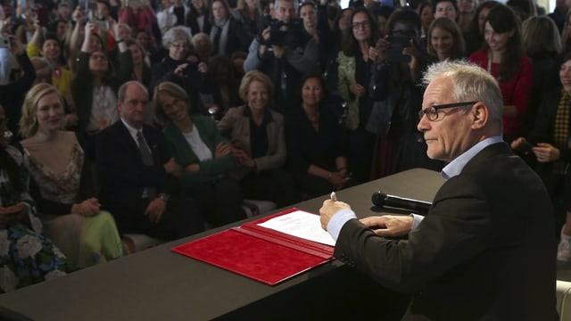 ein Mann unterschreibt an einer Pressekonferenz vor Journalisten ein Dokument. ein Mann unterschreibt an einer Pressekonferenz vor Journalisten ein Dokument.