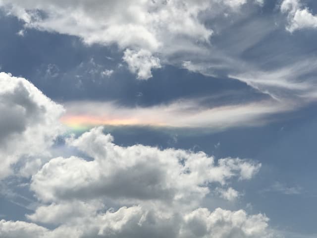 Leicht bewölkter Himmel mit Wolke, die an einen Regenbogen erinnert.