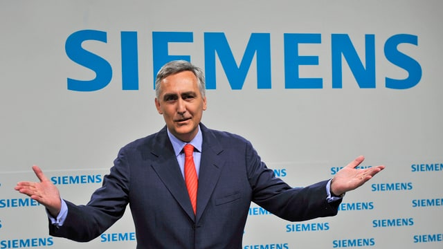 Ein Mann breitet die Arme vor einem Siemens-Firmenschild aus
