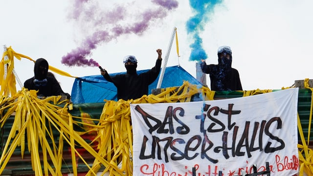 Besetzer mit Rauchfackeln, ein Transparent mit der Aufschrift "Das ist unser Haus". Besetzer mit Rauchfackeln, ein Transparent mit der Aufschrift "Das ist unser Haus".