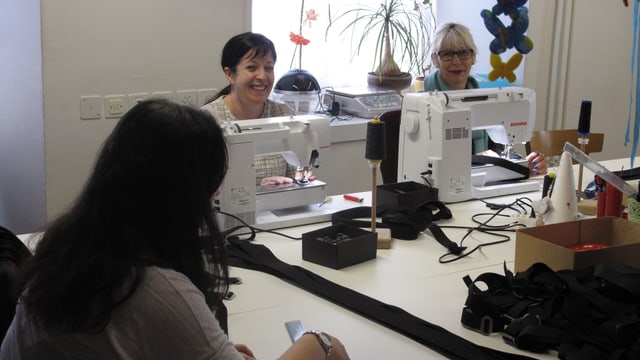 Zwei Frauen arbeiten an Nähmaschinen und schauen in die Kamera. Zwei Frauen arbeiten an Nähmaschinen und schauen in die Kamera.