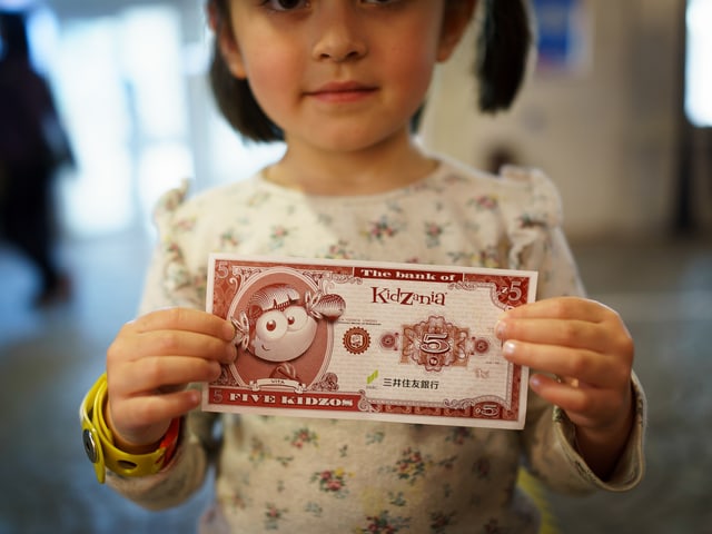 Ein Mädchen hält einen Spielgeldschein in die Kamera.