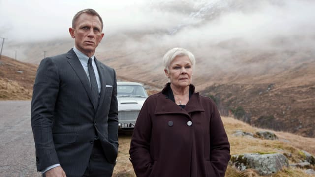 Ein Mann im Anzug und eine ältere Frau im Mantel stehen vor einem Auto in einer nebligen Landschaft. Ein Mann im Anzug und eine ältere Frau im Mantel stehen vor einem Auto in einer nebligen Landschaft.
