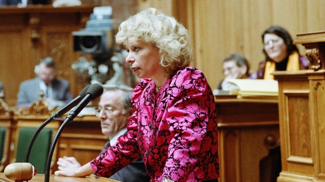 Frau mit blonden Haaren und rosarotem Blazer am Rednerpult im Schweizer Nationalrat Frau mit blonden Haaren und rosarotem Blazer am Rednerpult im Schweizer Nationalrat