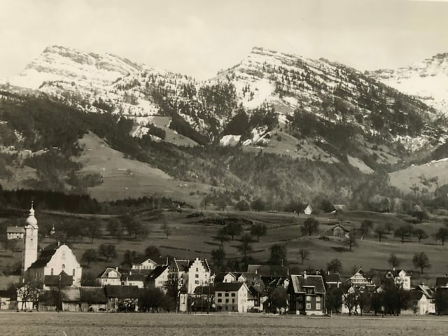 Altes Foto von kleinem Dorf vor Bergkulisse. 