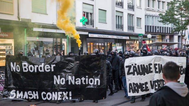 Schwarzvermummte Demonstranten halten ein schwarzes Transparent mit der Aufschirft: «No Border, No Nation. Smash Conex!» Schwarzvermummte Demonstranten halten ein schwarzes Transparent mit der Aufschirft: «No Border, No Nation. Smash Conex!»