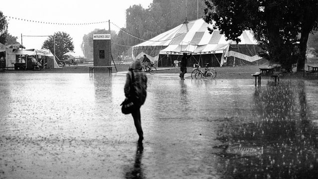 Eine Frau rennt im Regenschutz durch die Nässe. Eine Frau rennt im Regenschutz durch die Nässe.