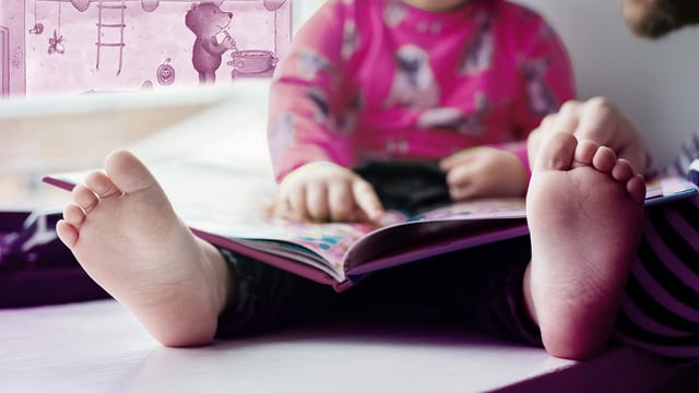 Kind schaut ein Bilderbuch an. Im Hintergrund eine Illustration eines Bären, der kocht. Kind schaut ein Bilderbuch an. Im Hintergrund eine Illustration eines Bären, der kocht.