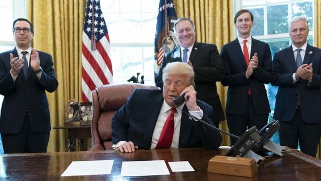 Trump am Telefon. Dahinter stehen Männer, die applaudieren. Trump am Telefon. Dahinter stehen Männer, die applaudieren.