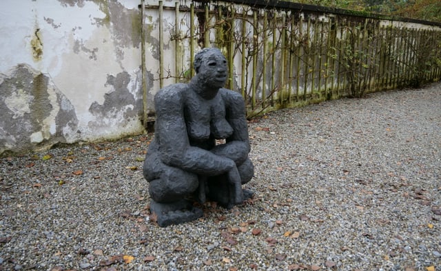 Eine Frauenfigur aus Stein kauert am Boden. Eine Frauenfigur aus Stein kauert am Boden.