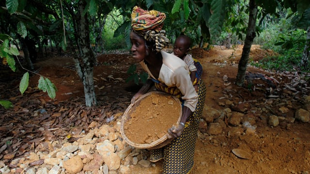 Eine Frau mit Kind trägt Sand, der auf Spuren von Gold untersucht werden soll. Eine Frau mit Kind trägt Sand, der auf Spuren von Gold untersucht werden soll.