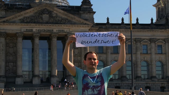Mann vor deutschem Bundestag mit Schrift: Volksentscheid - bundesweit. Mann vor deutschem Bundestag mit Schrift: Volksentscheid - bundesweit.