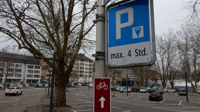 Parkplatz. Parktafel im Vordergrund. Hinten ein wenig besetzter Parkplatz. Parkplatz. Parktafel im Vordergrund. Hinten ein wenig besetzter Parkplatz.