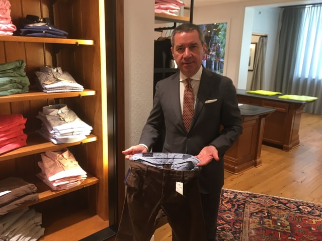 Franco Savastano zeigt eine Hose neben einem Gestell mit Herrenkleidern. Franco Savastano zeigt eine Hose neben einem Gestell mit Herrenkleidern.