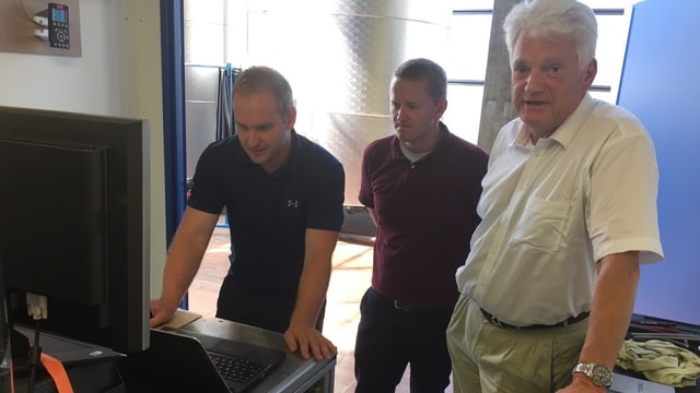 Drei Männer stehen um einen Computer herum. Drei Männer stehen um einen Computer herum.
