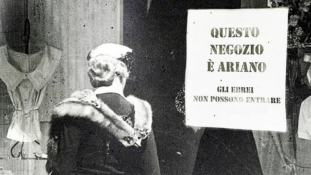 Italien, 1983: Eine Frau steht vor einem Laden. Auf dem Schaufenster hängt ein Schild. Darauf steht «Dieser Laden ist arisch». Italien, 1983: Eine Frau steht vor einem Laden. Auf dem Schaufenster hängt ein Schild. Darauf steht «Dieser Laden ist arisch».