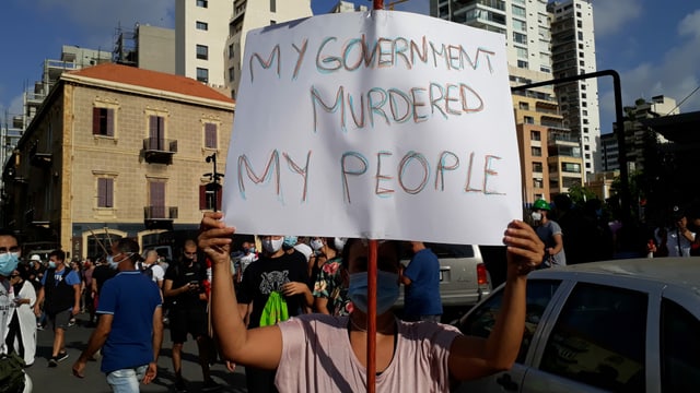 Frau hält Schild in die Höhe: "Meine Regierung hat mein Volk ermordet."