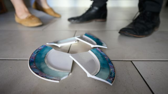 Ein zerbrochener Teller vor einem streitenden Paar Ein zerbrochener Teller vor einem streitenden Paar