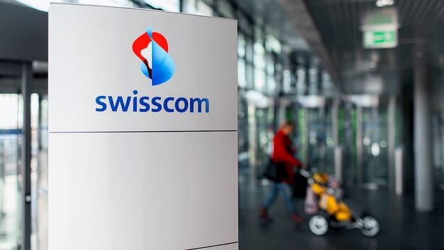zwei beleuchtete Swisscom-Logos, eines davon spiegelt sich in der Glastür eines Gebäudes zwei beleuchtete Swisscom-Logos, eines davon spiegelt sich in der Glastür eines Gebäudes