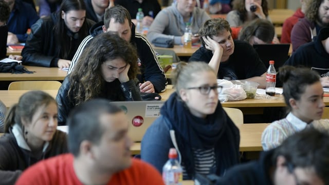 Junge Männer und Frauen sitzen in Reihen an Tischen Junge Männer und Frauen sitzen in Reihen an Tischen