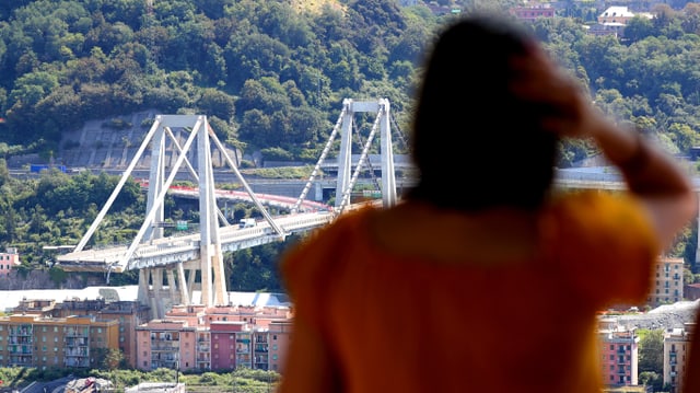 Bild der eingestürzten Brücke. Im Vordergrund eine Frau, die sich an den Kopf fasst. Bild der eingestürzten Brücke. Im Vordergrund eine Frau, die sich an den Kopf fasst.