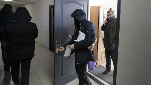 Polizisten tragen Dokumente und Computer aus dem Büro des weissrussischen Journalistenverbandes, während Andrei Bastunets, der Leiter des Verbandes, rechts, im Büro in Minsk, Belarus, steht, Dienstag, 16. Februar 2021 Polizisten tragen Dokumente und Computer aus dem Büro des weissrussischen Journalistenverbandes, während Andrei Bastunets, der Leiter des Verbandes, rechts, im Büro in Minsk, Belarus, steht, Dienstag, 16. Februar 2021
