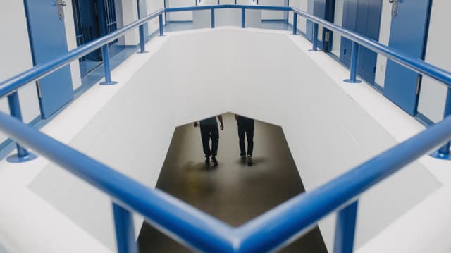 Blick durch eine Öffnung im Boden auf ein tieferliegendes Stockwerk. Dort gehen zwei Personen nebeneinander. Blick durch eine Öffnung im Boden auf ein tieferliegendes Stockwerk. Dort gehen zwei Personen nebeneinander.