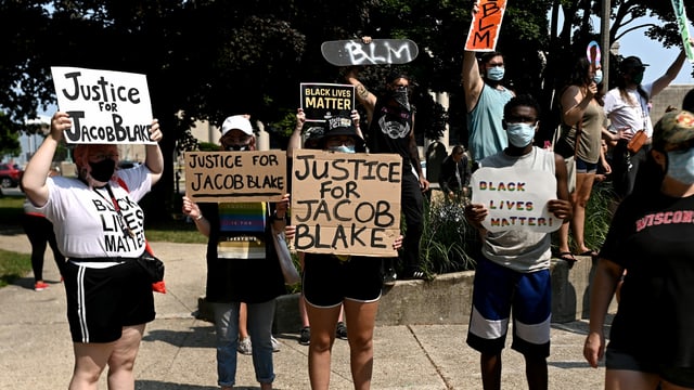 Menschen halten Plakate hoch mit der Aufschrift: "Justice for Jacob Blake" und "Black Lives Matter". Menschen halten Plakate hoch mit der Aufschrift: "Justice for Jacob Blake" und "Black Lives Matter".