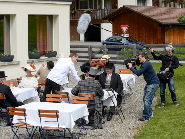 Gartenterrasse, Thalers und andere Statisten sitzend an Tischen, Kameraleute filmen