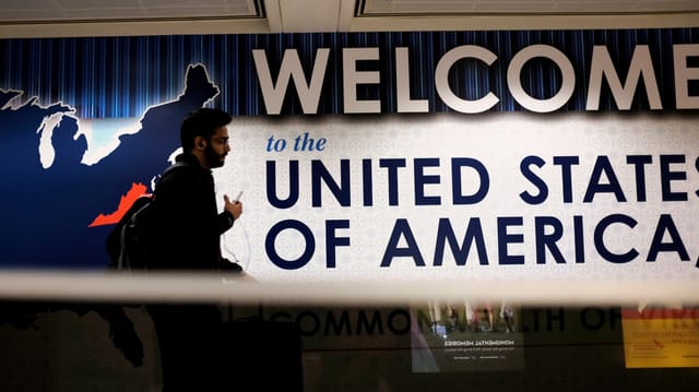 Mann läuft am Flughafen an einem Schild vorbei mit der Aufschrift: Willkommen in den vereinigeten Staaten von Amerika. Mann läuft am Flughafen an einem Schild vorbei mit der Aufschrift: Willkommen in den vereinigeten Staaten von Amerika.