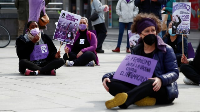 Frauen mit violetter Kleidung sitzen auf einem Platz.