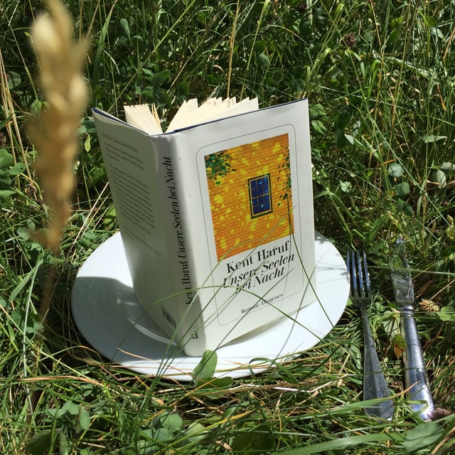 Das Buch «Unsere Seelen bei Nacht» von Kent Haruf steht aufrecht aufgeschlagen auf einem weissen Teller im Gras Das Buch «Unsere Seelen bei Nacht» von Kent Haruf steht aufrecht aufgeschlagen auf einem weissen Teller im Gras