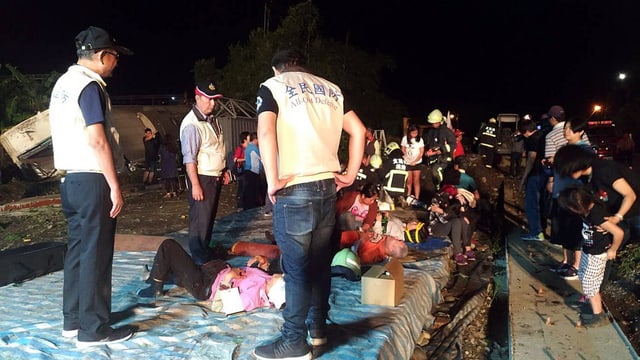Rettungskräfte stehen um Verletzte. Im Hintergrund der verunglückte Zug. Rettungskräfte stehen um Verletzte. Im Hintergrund der verunglückte Zug.