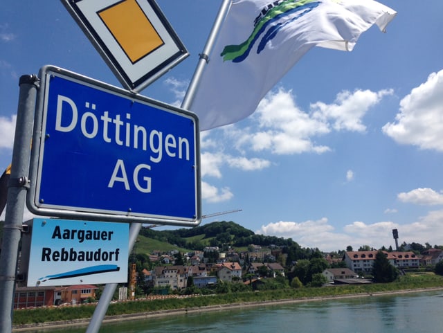Ortschild Döttingen vor Fluss, im Hintergrund sind Häuser. Ortschild Döttingen vor Fluss, im Hintergrund sind Häuser.
